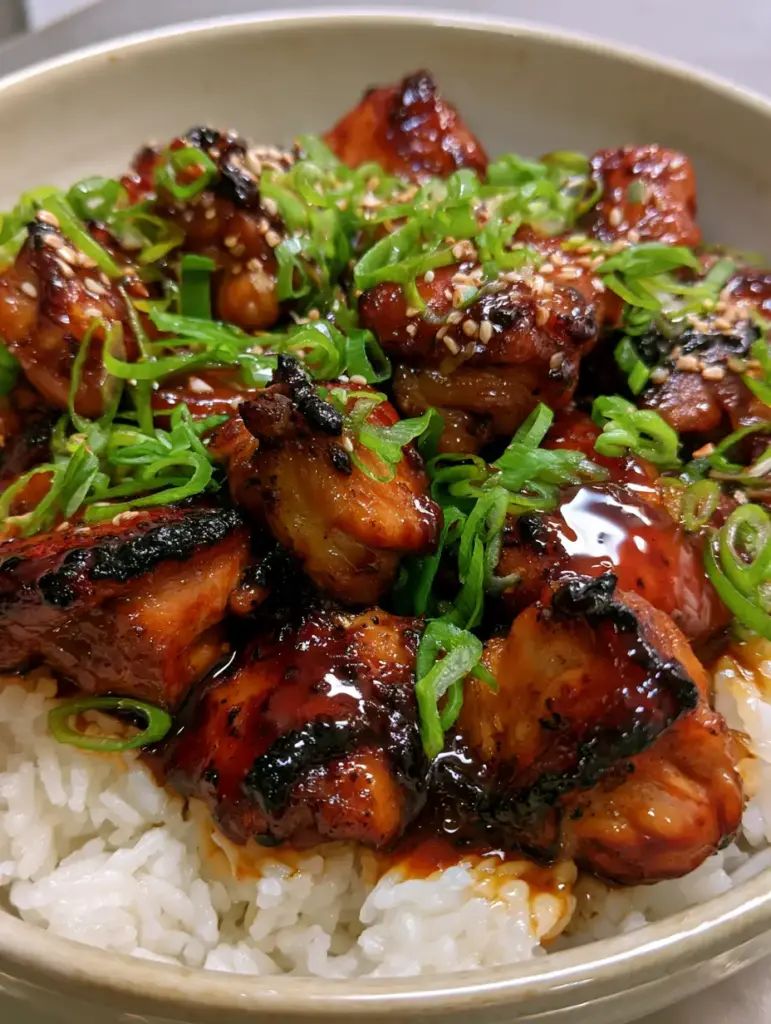 Smartphone photo of bourbon chicken heavily garnished with green scallions and sesame seeds over jasmine rice.
