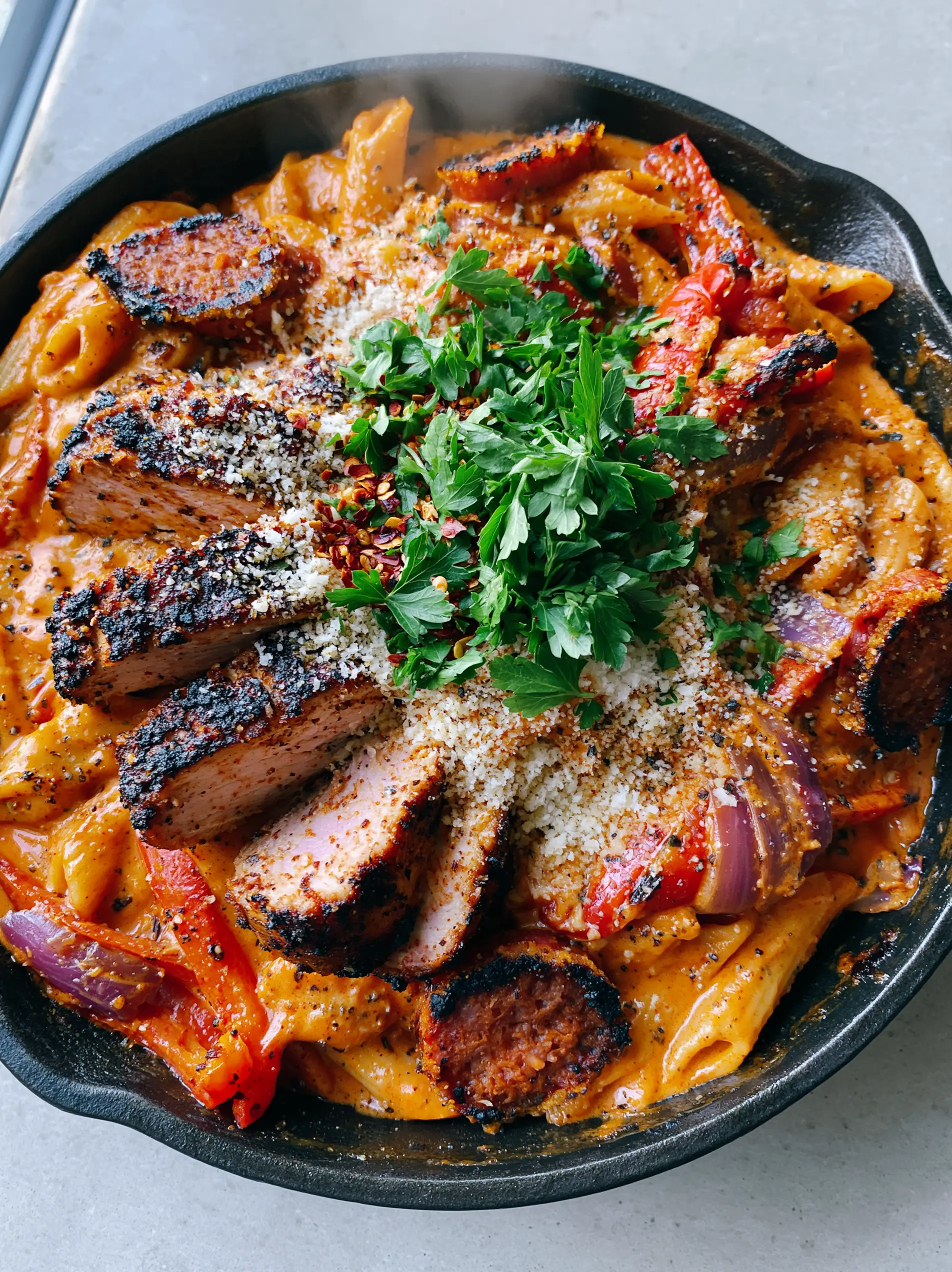 Close up shot of al dente penne in a thick, vibrant orange-red cream sauce with visible flecks of black pepper.