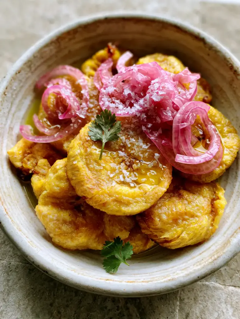 Top-down view of pale buttery yellow Boiled Green Plantains in a rustic white bowl.