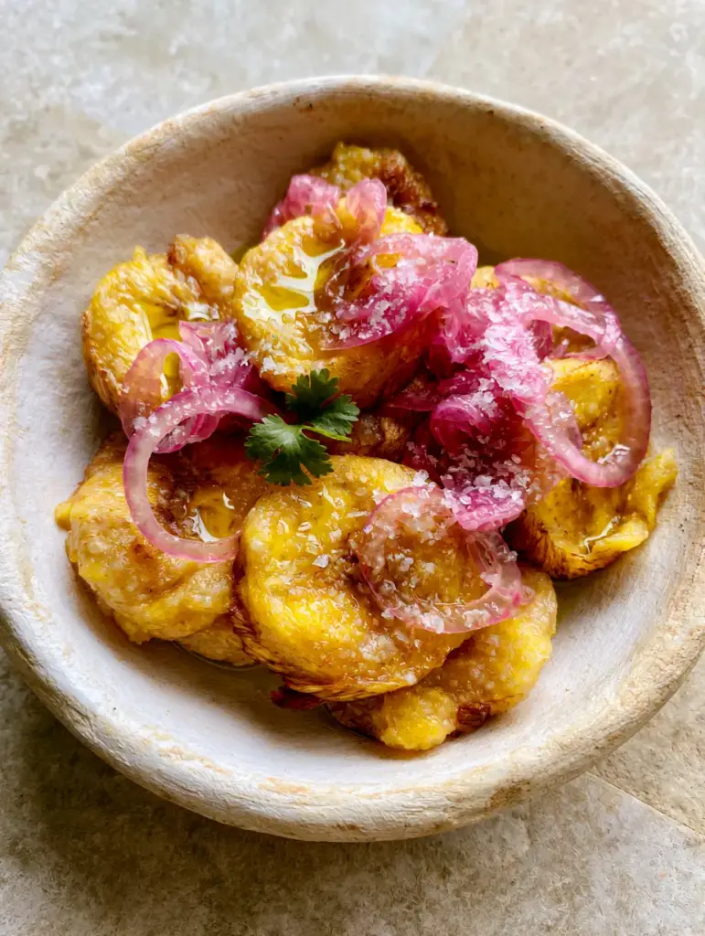 Close-up of translucent pickled red onions and sea salt flakes on Boiled Green Plantains.