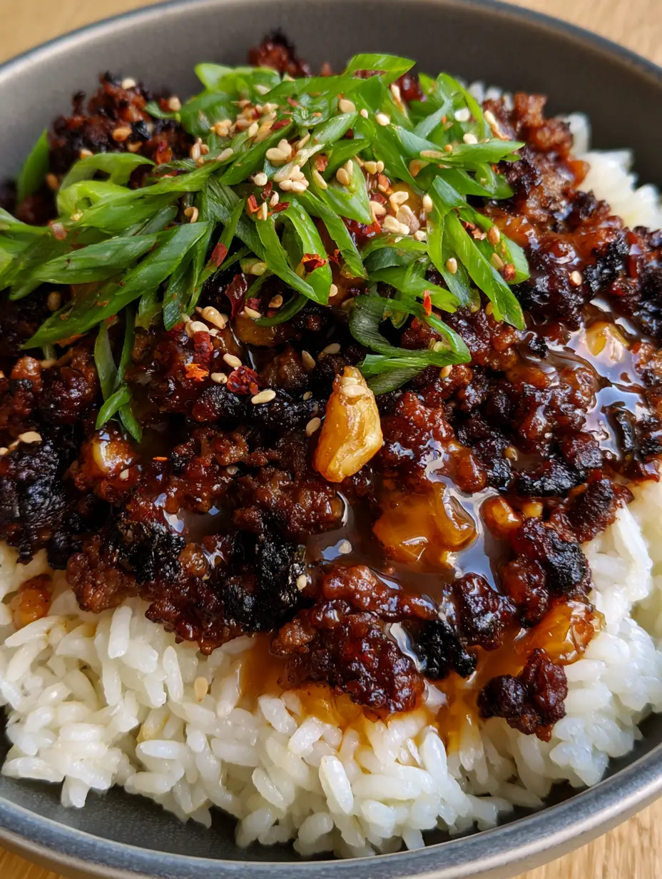 Close-up of crispy seared beef with honey garlic sauce and bias-cut scallions in a charcoal bowl.
