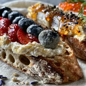 Extreme close-up of three gourmet French tartines featuring whipped creme fraiche, brie, and salmon roe. (Bastille Day recipes)