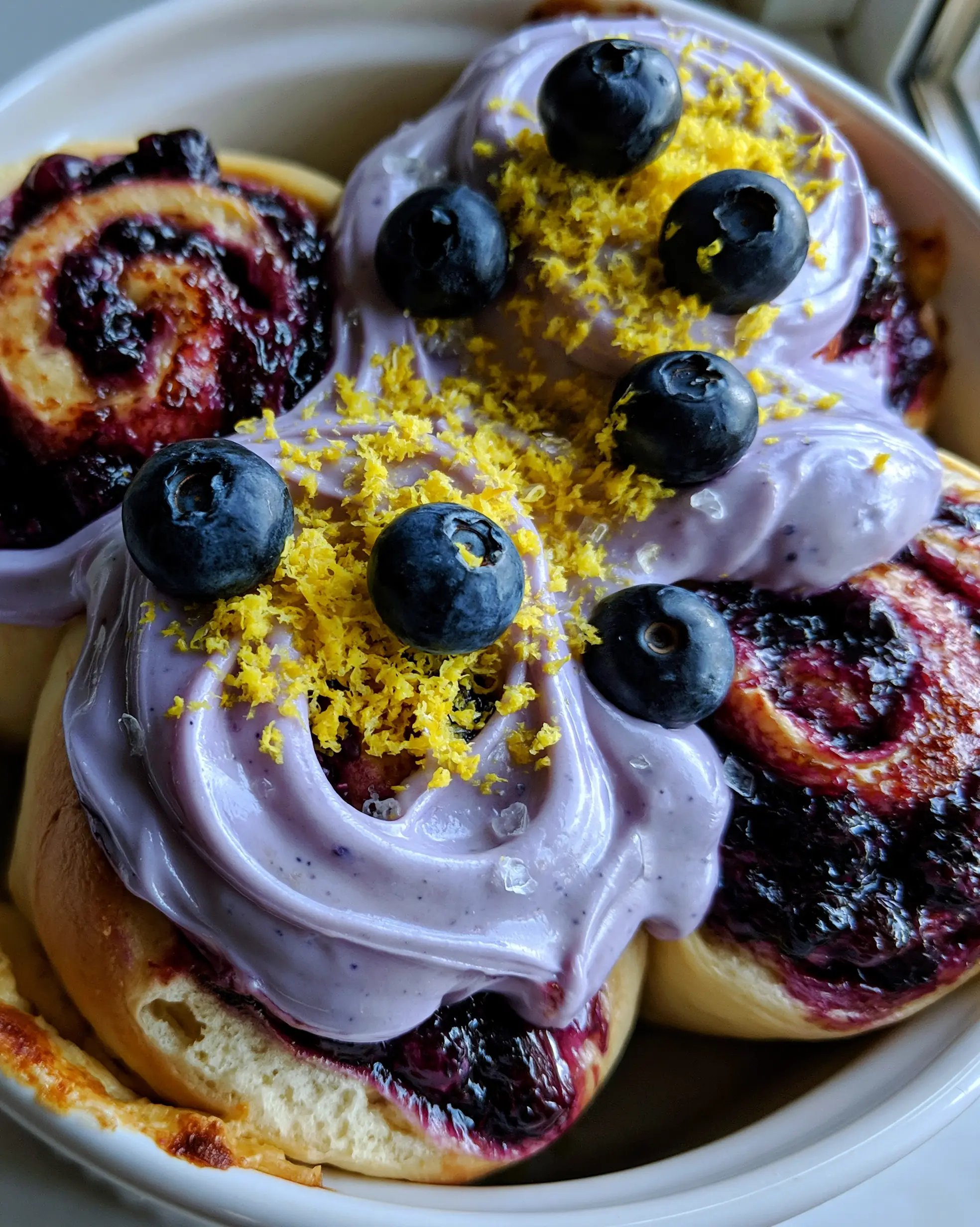 Macro top-down view of six oversized blueberry cinnamon rolls in a white baking dish with glossy lavender swirls. (blueberry cinnamon rolls)