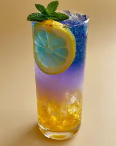 Close-up of sparkling water bubbles and crushed ice in a Honey Lemon Butterfly Fizz mocktail with a pastel lavender gradient.