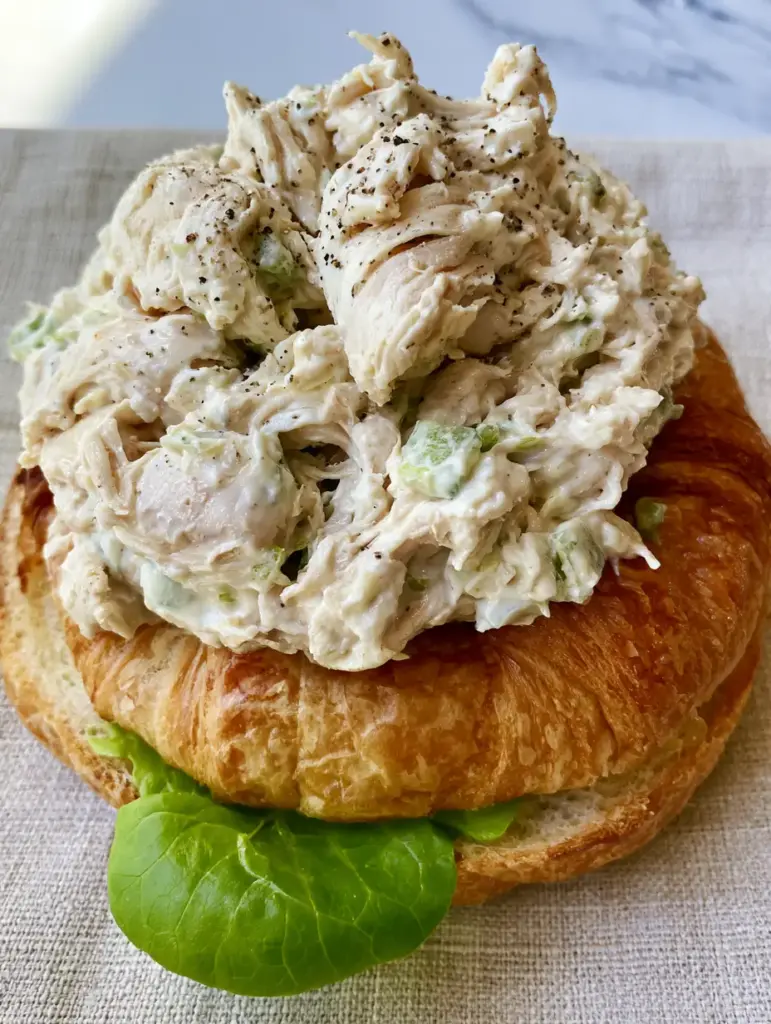 A handheld smartphone photo of a golden toasted croissant filled with signature chicken salad.